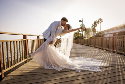 BRide and groom kissing on  a board walk by the beach at a malaga wedding venue