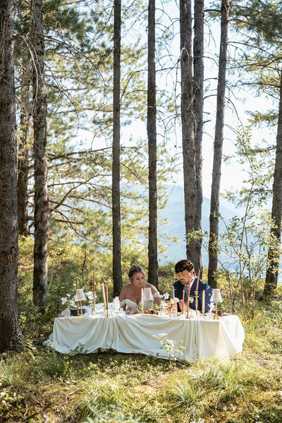 ewlywed couple enjoying an intimate dinner in the woods after their elopement, surrounded by soft candlelight, draped linens, and mountain views.