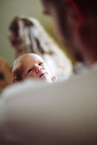 Newborn baby looking up at Dad, picture taken from over Dad's shoulder by lifestyle newborn photographer in Tifton