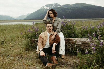 Couple sitting on the ground next to a field of lupines in Girdwood, Alaska