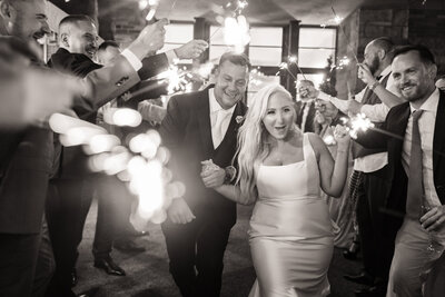 Newlyweds make a joyful sparkler exit, surrounded by cheering guests and glowing lights.