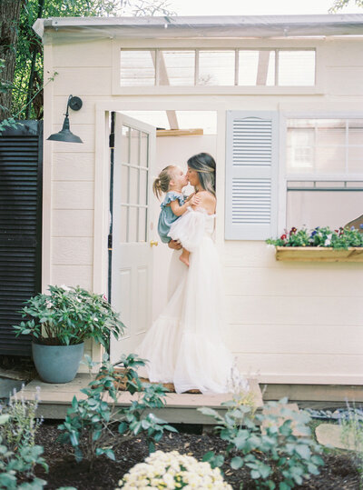 A mother holds her young daughter while standing in a doorway and gives her a kiss during her Maryland family session