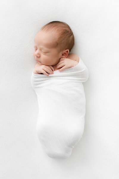 A photo of a sweet baby sleeping on a white blanket in a white swaddle by Washington DC Family Photographer