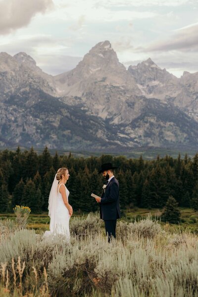 groom holding bride next to a lake with low mountains in the background