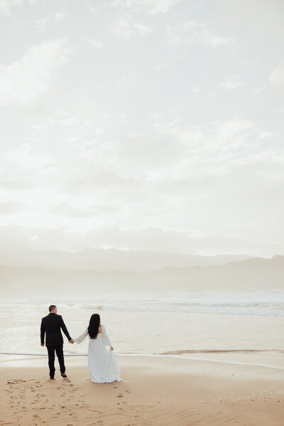 Bride and groom holding hands walking on hawaiian beach