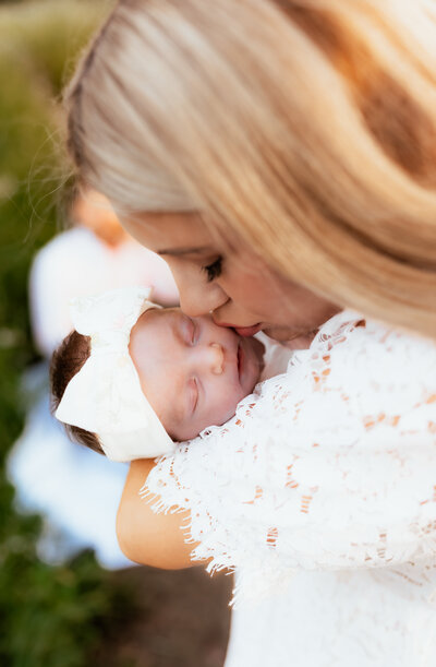 A mother in white holding and kissing her newborn baby girl on the cheek. 