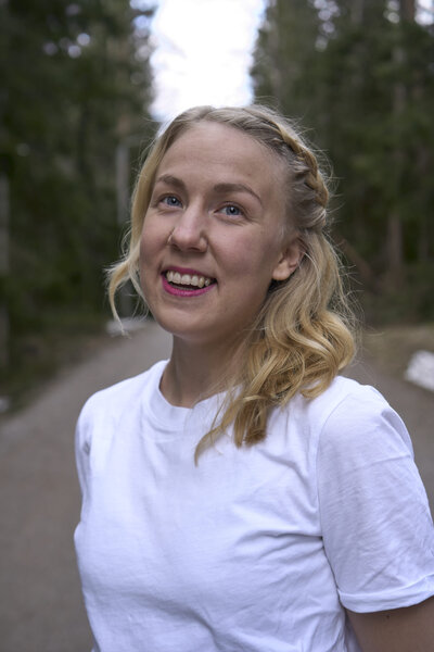 mielen paremminvoinnin ja kehomieliyhteyden valmentaja hymyilee kameralle metsätiellä