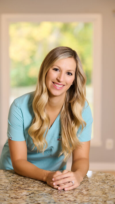 a blonde woman in scrubs leaning on a counter while smiling