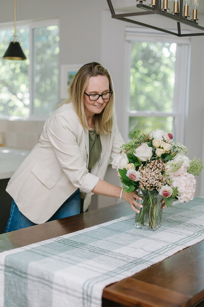 Kim Kussman, Utah Realtor & Owner of Nurture Lane, arranging flowers in a dining room of a realty listing