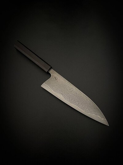 A chef's knife with a dark handle and a damascus steel blade featuring intricate patterns, displayed on a dark surface.