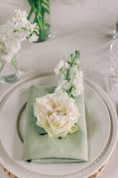 Close-up photo of a table setting with white plates, green napkins and white flowers