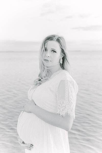 Meirdian Idaho Glowing expectant mother in a flowing, light-colored dress, cradling her baby bump in a sunlit outdoor setting.