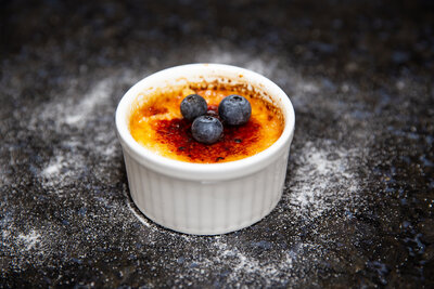 Silky smooth crème brûlée with a perfectly caramelized sugar crust, offering a rich and creamy finish to your meal. Shown served with Blueberries.