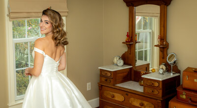 A bride wearing an off the shoulder dress looks over her shoulder and smiles at Slyvanside Farms
