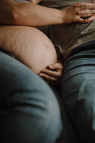 Artistic picture of pregnant moms belly laying next to dad while holding hands in a moody studio in Severn, Maryland.