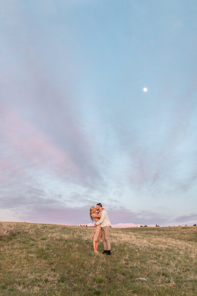 Man and woman kiss while holding one another in a field.