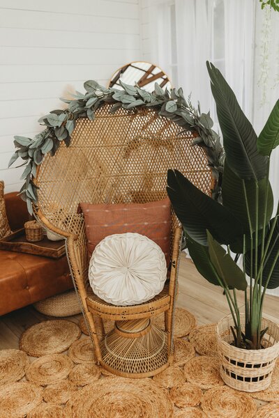 Wicker chair with boho pillows and greenery surrounding it.