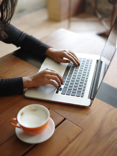 cropped-hand-woman-using-laptop-with-coffee-table