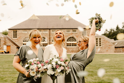Bride and bridesmaids laughing under confetti at aswanley wedding venue