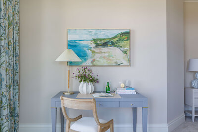 A blue desk with a painting of a beach just above hanging from the wall.