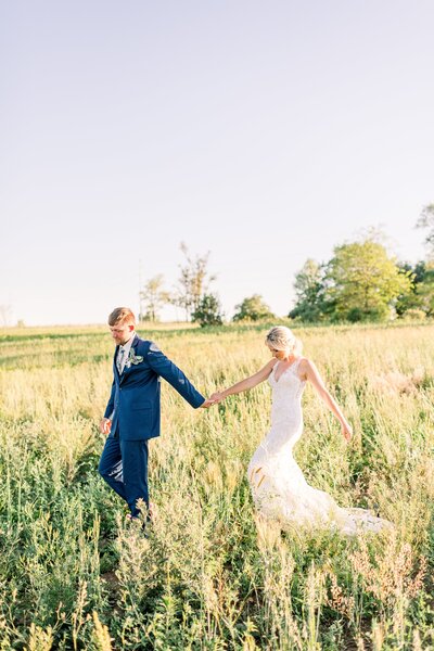Photo of married couple holding hands while walking through the prairie grass at The Eloise
