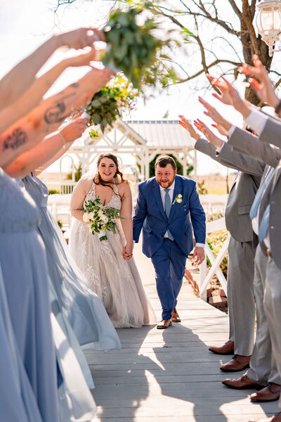 A joyful wedding party gathered in a rustic barn, making a tunnel for the bride and groom to run through.
