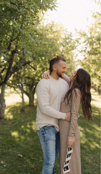 A man and woman are smiling at each other. Her arm is around his neck and his hand is around her waist.