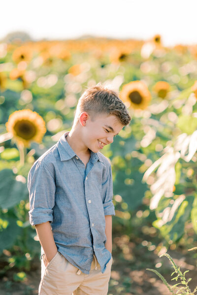 Young boy in a sunflower field looking down and laughing