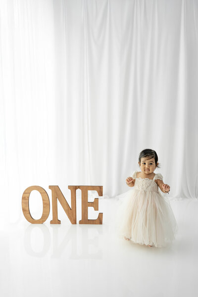 Girl in dress standing next to large ONE during a cake smash session— captured by Alliston and Barrie cake smash photographer.