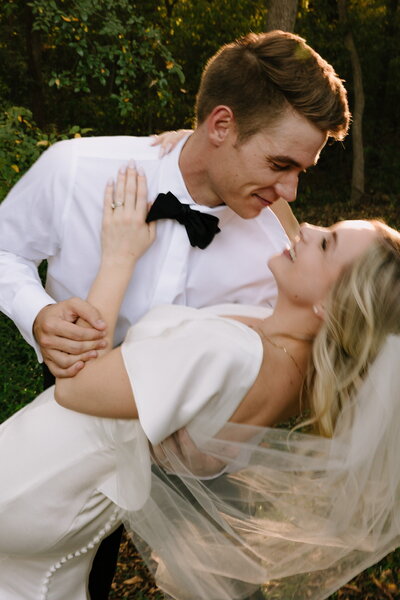 Groom dressed in a white shirt and black bowtie dips his new wife.