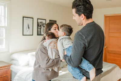 father holding his son kissing her mother that's also holding a newborn