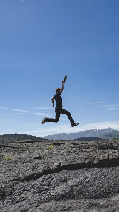 Man jumps holding camera over rocky crater