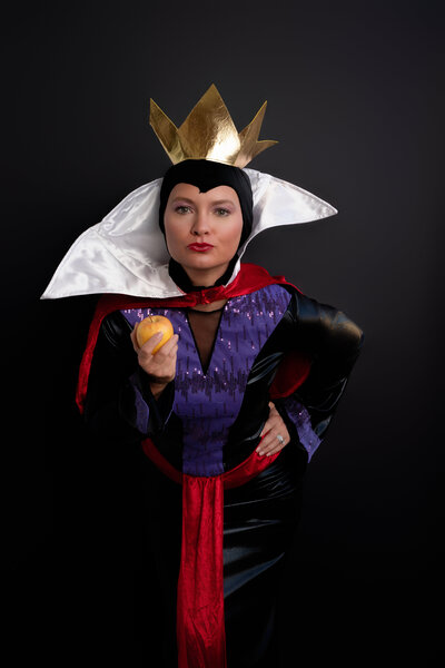 Woman dressed as Snow White's Evil Queen holding an apple with a slight smirk on her face. Halloween Costume portrait Holly Springs, NC