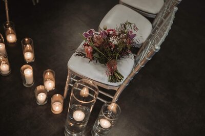 A vibrant floral bouquet rests on a silver chiavari chair at SoHo63, a Chandler wedding and event venue. Surrounded by glass cylinders with floating candles, the scene captures a quiet, romantic moment before the ceremony begins.