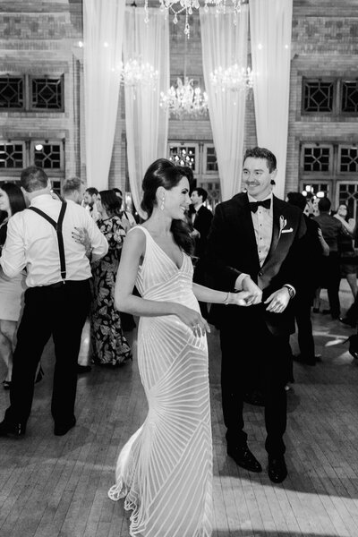 A candid black and white wedding photo of a bride and groom sharing a joyful moment on the dance floor at Café Brauer, capturing the energy of their reception.