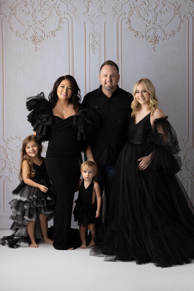 A stylish family portrait featuring a mother, father, two daughters, and a toddler in chic black gowns and clothing, created by a Dallas family photographer.