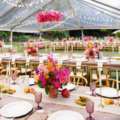 Colorful floral arrangements on wedding reception tables under a clear tent 