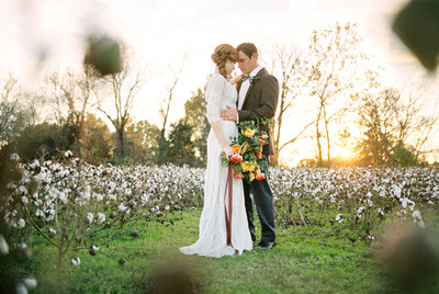Bride and groom embrace in cotton field holding bouquet