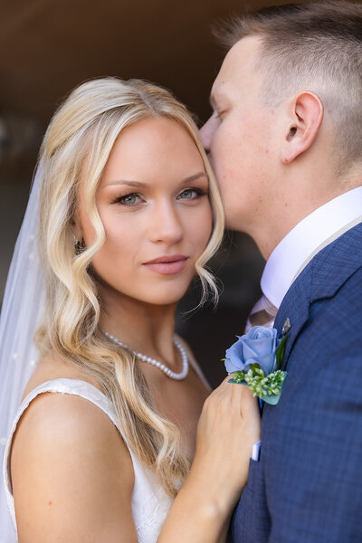 bride looking at camera with groom kissing her head
