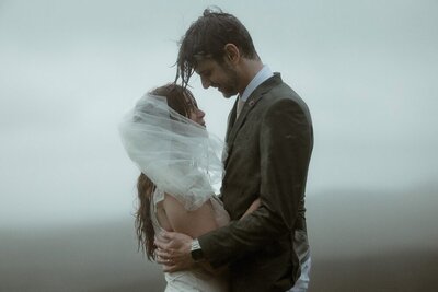 A bride and groom stare into each others eyes during a rain storm on their wedding day on the Isle of Skye, Scotland