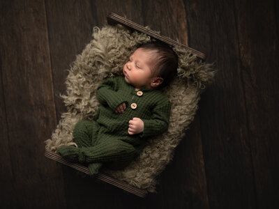 newborn baby boy in green outfit posed on bed for newborn portraits