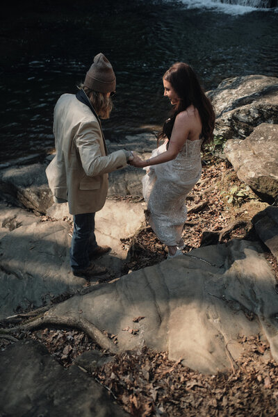 Couple helping each other down rocks in wedding attire