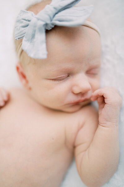 Newborn sleeping baby's face and upper chest, gently rests her hand near her face, while wearing a soft blue headband by Portland Newborn Photographer Emilie Phillipson Photography.