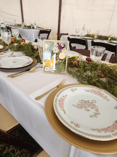 A thrifted wedding table scape including plates, chargers, flatware, table numbers and greenery. 