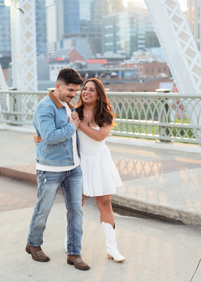 a latino catholic couple laugh and walk along the iconic pedestrian bridge in downtown nashville, tn during their Downtown Nashville Engagement Session