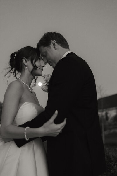 couple standing together in an embrace as the full moon shines down behind them 
