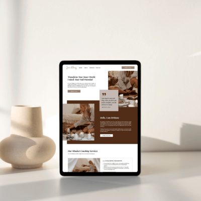 Tablet displaying a mindset coaching service website with a warm brown color scheme, set on a minimalist desk with neutral decor