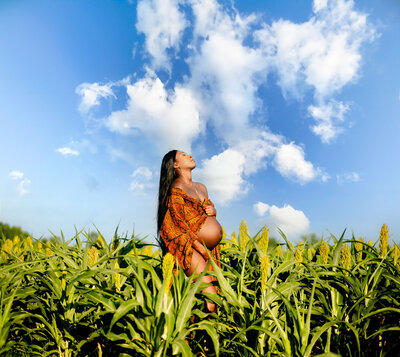 Black Woman maternity shoot with long black hair wearing a snakeskin sheer robe with belly visible in a corn field