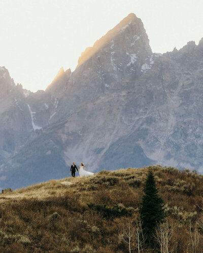 bride and groom walking over ridge with mountains in the background