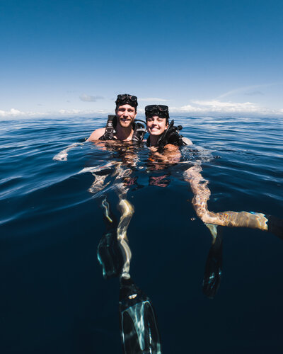 Two scuba divers swim in the water at the surface with their goggles on their foreheads